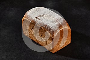 Whole loaf of fresh, delicious baked white bread sprinkled with flour. Black background with copy space. Close-up