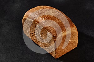 Whole loaf of fresh, palatable baked white bread against black background with copy space. Close-up