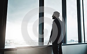 On a whole new level. Shot of a young businessman looking thoughtfully out of an office window.