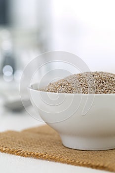 Whole, organic white chia seeds heap in white bowl with bright kitchen background - selective focus