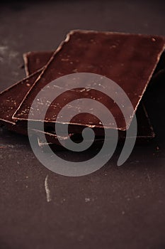 Whole and pieces of dark chocolate bars on a darkbackground at