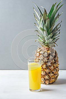 Whole Pineapple Tall Glass with Freshly Pressed Orange Citrus Juice on White Kitchen Table Grey Stone Wall. Vitamins Morning