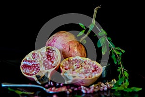 whole pomegranate fruit cut in half and its leaves on a wooden table, spoon with fruit grains next to it