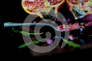 whole pomegranate fruit cut in half and its leaves on a wooden table, spoon with fruit grains next to it