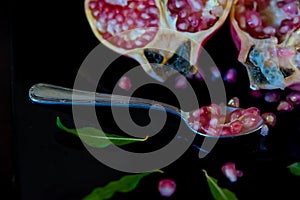 whole pomegranate fruit cut in half and its leaves on a wooden table, spoon with fruit grains next to it