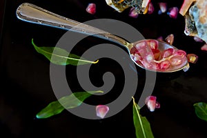 whole pomegranate fruit cut in half and its leaves on a wooden table, spoon with fruit grains next to it