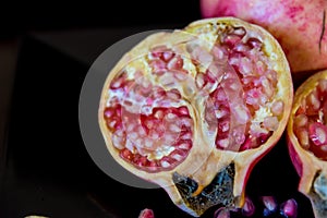 whole pomegranate fruit cut in half and its leaves on a wooden table, spoon with fruit grains next to it