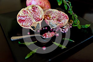 whole pomegranate fruit cut in half and its leaves on a wooden table, spoon with fruit grains next to it