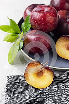 Whole purple plums and slices with leaves and knife on ceramic plate, light grey concrete background