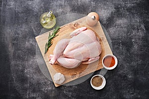 Whole raw chicken on wooden board on dark background. Preparing raw chicken. Top view