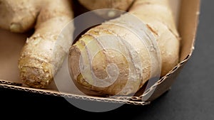 Whole raw ginger root or rhizome in paper packaging on a black background