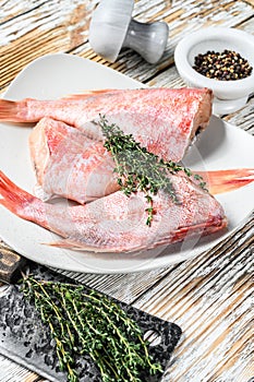 Whole raw red snapper fish on a plate. White wooden background. Top view