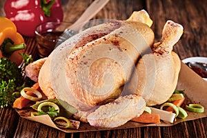 Whole raw seasoned chicken with fresh vegetables photo