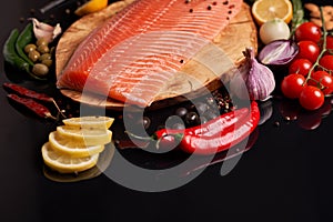 Whole red fish fillet on a wooden plate with cherry tomatoes, red and green chili peppers, black and green olives, lemon, garlic,