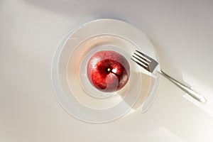 Whole ripe red apple on a white plate with fork. Isolated on white background. Ready to healthy eating. Raw food diet.