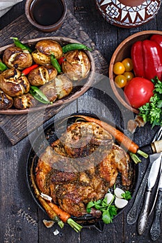 Whole roast chicken in an iron pan on dark background, top view.