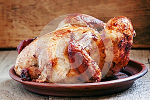 Whole roast chicken with a ruddy crust on a clay dish on the old