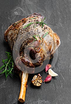 Whole roast lamb leg on black stone background