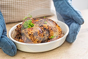 Whole roasted chicken in a baking bowl holding in hands cook with gloves