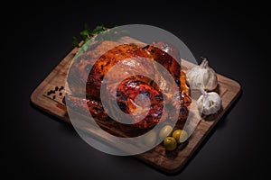 Whole roasted chicken on cutting board with vegetables over black background