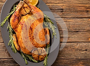 Whole roasted chicken with lemon and rosemary on a black plate. Rustic style. Christmas concept. Christmas turkey.