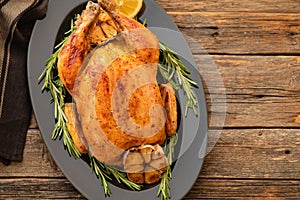 Whole roasted chicken with lemon and rosemary on a black plate. Rustic style. Christmas concept. Christmas turkey.