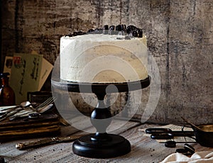 Whole round cake with white cream, black cookies on black wooden cake stand