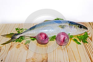 Whole round fish yellowtail and red onion on a wooden surface