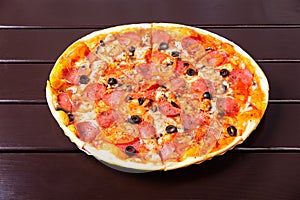 A whole rustic pizza with mozzarella, salami, tomato, olives, mushrooms and basil