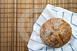 Whole rye bread placed on white cloth with blue stripe.