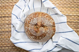 Whole rye bread placed on white cloth with blue stripe over wicker texture.