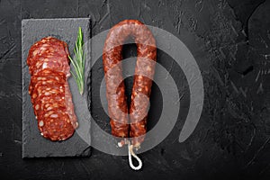 Whole and sliced chorizo sausage on black background, flat lay with copy space