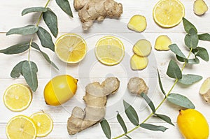 Whole and sliced fresh lemon, ginger root, eucalyptus leaves on white wooden background. Flat lay top view copy space. Minimal