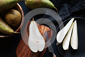 Whole and sliced ??ripe pears on a wooden board and plates on a dark background