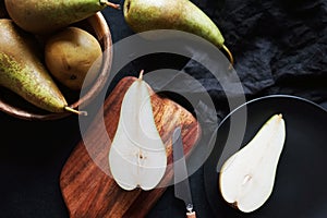 Whole and sliced ??ripe pears on a wooden board and plates on a dark background