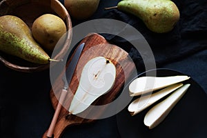 Whole and sliced ??ripe pears on a wooden board and plates on a dark background