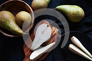 Whole and sliced ??ripe pears on a wooden board and plates on a dark background