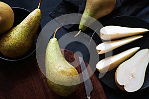 Whole and sliced ??ripe pears on a wooden board and plates on a dark background
