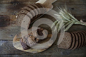Whole and sliced â€‹â€‹rye bread with sesame seeds and ears of rye on a wooden rustic background. Flat lay.