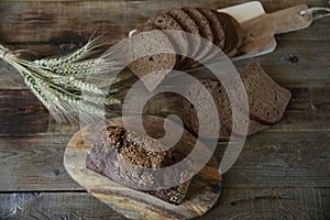 Whole and sliced â€‹â€‹rye bread with sesame seeds and ears of rye on a wooden rustic background. Flat lay. Top view.