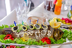 Whole stuffed fish on an oblong dish, decorated with lemon, vegetables and olives. A traditional Jewish dish or banquet dish.