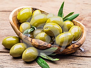 Whole table olives in the wooden bowl on the table.