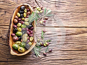 Whole table olives in the wooden bowl on the table.