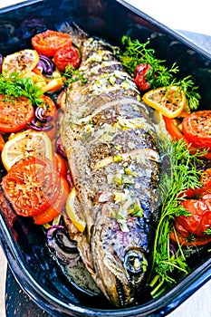 Whole trout with vegetables and dill on a black tray, vertical