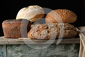 whole various baked rye flour bread rolls on an old wooden table