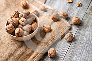 Whole walnuts in a bowl and jute bag on rustic old wooden table.