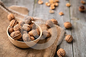 Whole walnuts in a bowl and jute bag on rustic old wooden table. photo