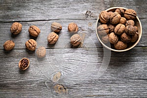 Whole walnuts in a bowl and on rustic old wooden table. photo