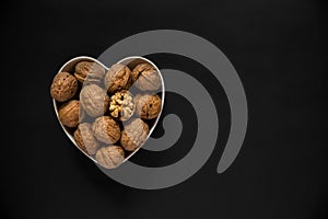 Whole walnuts and one cracked broken heart in a white heart-shaped bowl on a black background