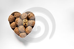 Whole walnuts and one cracked broken heart in a white heart-shaped bowl on a white background